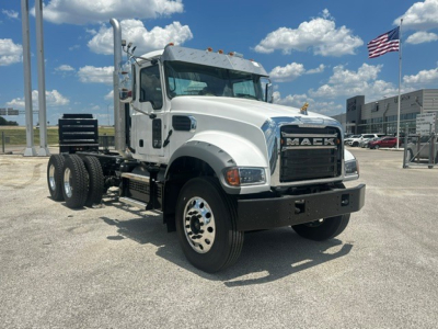 Mack GR64F cab and chassis truck side view showing front grille with MACK logo, dual rear axles, white cab, black bumper, and American flag in background.
