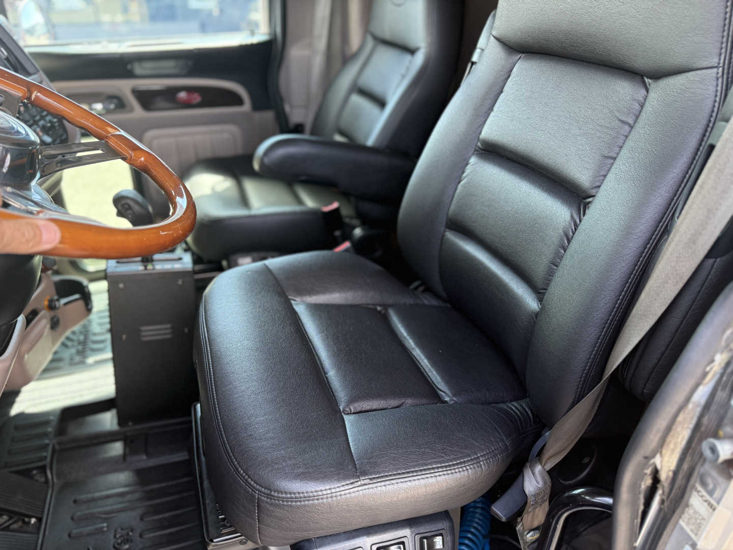 Cab interior of a 2022 Peterbilt 389 with black leather seats, steering wheel, and driver area visible.