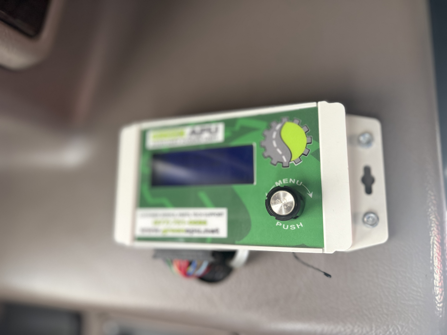 Green control module mounted on a panel with a small display, a circular button labeled MENU PUSH, and warning labels.