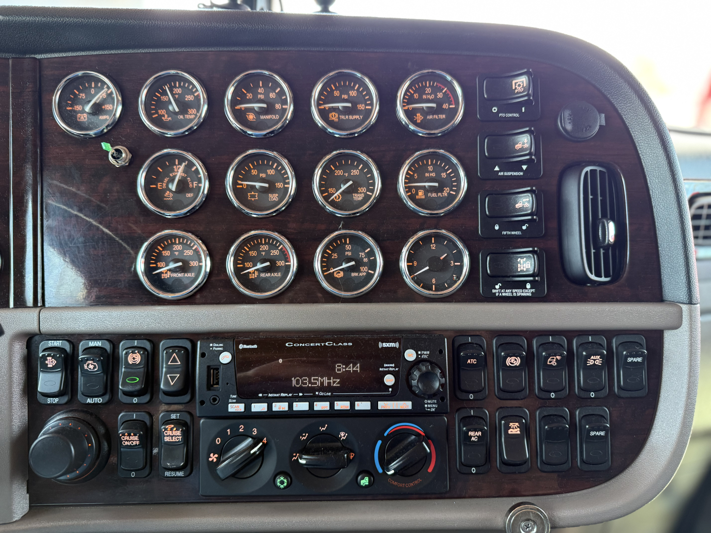 Peterbilt 389 dash cluster with multiple gauges and controls; radio display shows 103.5 MHz; various switches; no visible VIN or stock data.