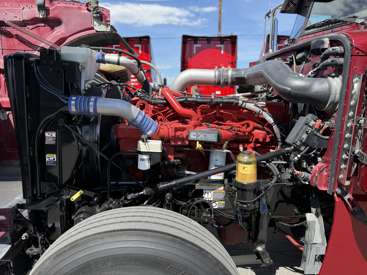 Peterbilt 389 truck engine bay showing red engine with EX15 badge, hoses, filters, and components.