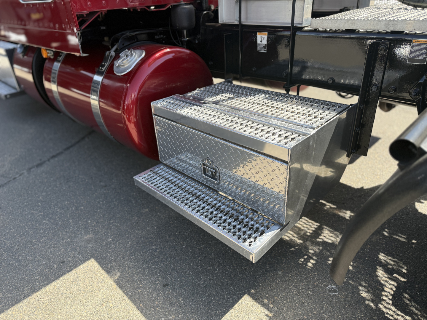 Peterbilt 389 side: diamond-plate aluminum steps under cab, fuel tank behind, part of chassis visible