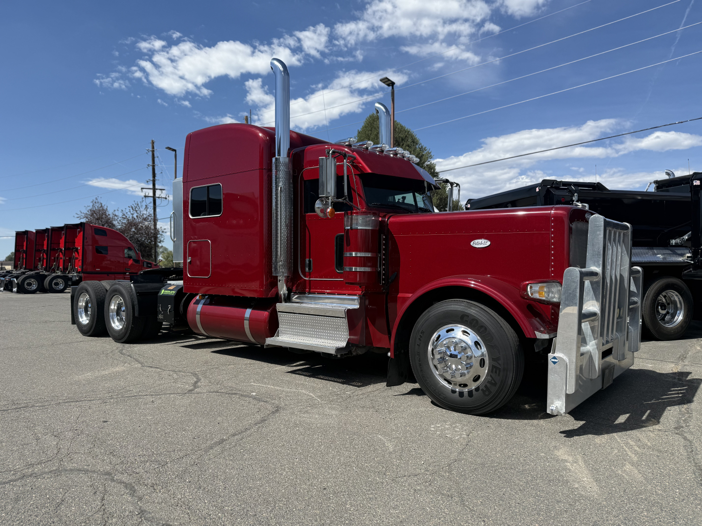 Peterbilt 389 truck in red, side view showing chrome exhaust stacks, silver front bumper, large fuel tanks, and dual rear axles.