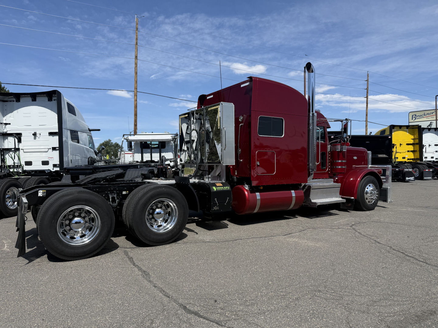 2022 Peterbilt 389 tractor cab side view showing sleeper with maroon paint, dual rear axles, chrome exhaust stacks, fuel tanks, and side windows.