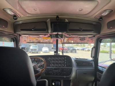 Peterbilt 389 cab interior view showing dashboard gauges and steering wheel with overhead mirror and windshield.