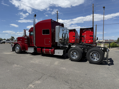 Peterbilt 389 conventional sleeper truck side view showing red cab and chassis, dual rear axles, chrome exhaust stacks, sleeper compartment, and trailer hitch area.