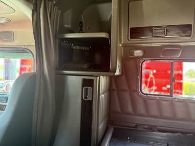 Peterbilt truck cabin interior showing a storage cabinet with a small door, window to the outside, and vertical black trim; seating area visible