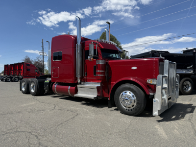 Peterbilt 389 truck in red, side view showing chrome exhaust stacks, silver front bumper, large fuel tanks, and dual rear axles.