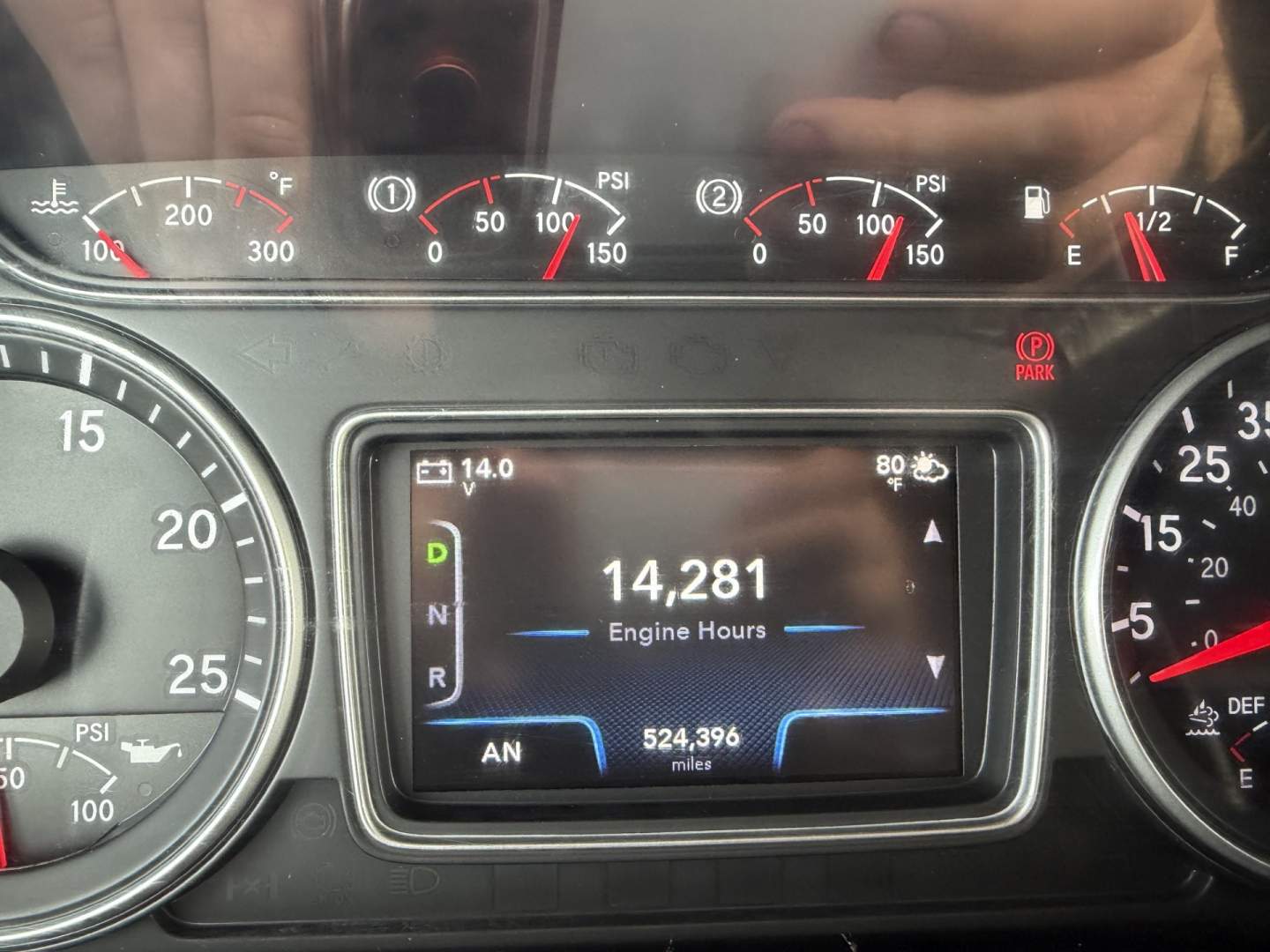 Instrument cluster and digital display in a truck cab showing engine hours 14,281 and 524,396 miles. Various gauges with PSI and temperature indicators visible around the display.