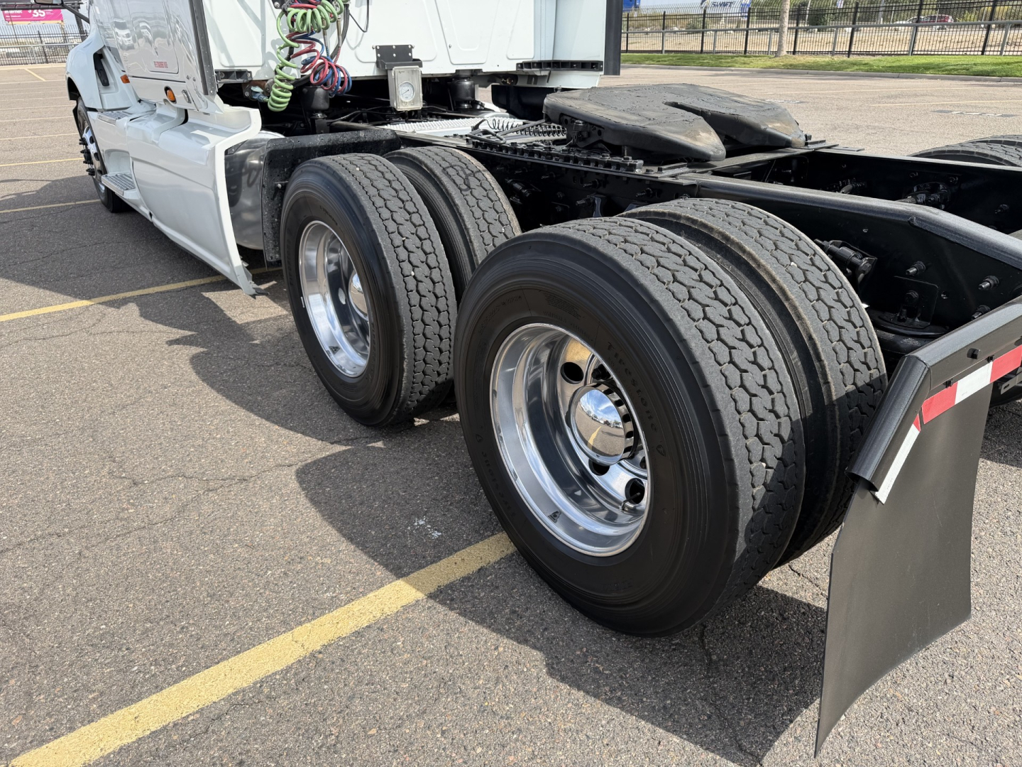 Truck rear chassis with dual rear axles and wheel tires, white cab, chrome rims, and black mud flaps visible.