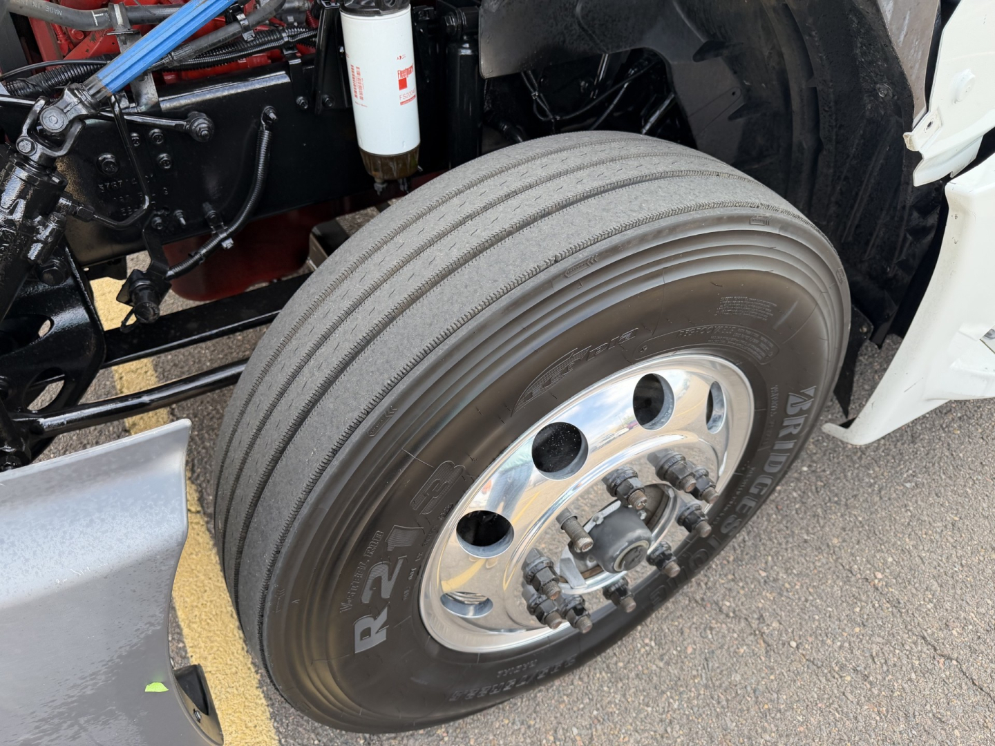 Truck front wheel and suspension detail with tire label 'R' and alloy rim; visible components include air filter canister, blue hose, metal frame, and wheel hub.