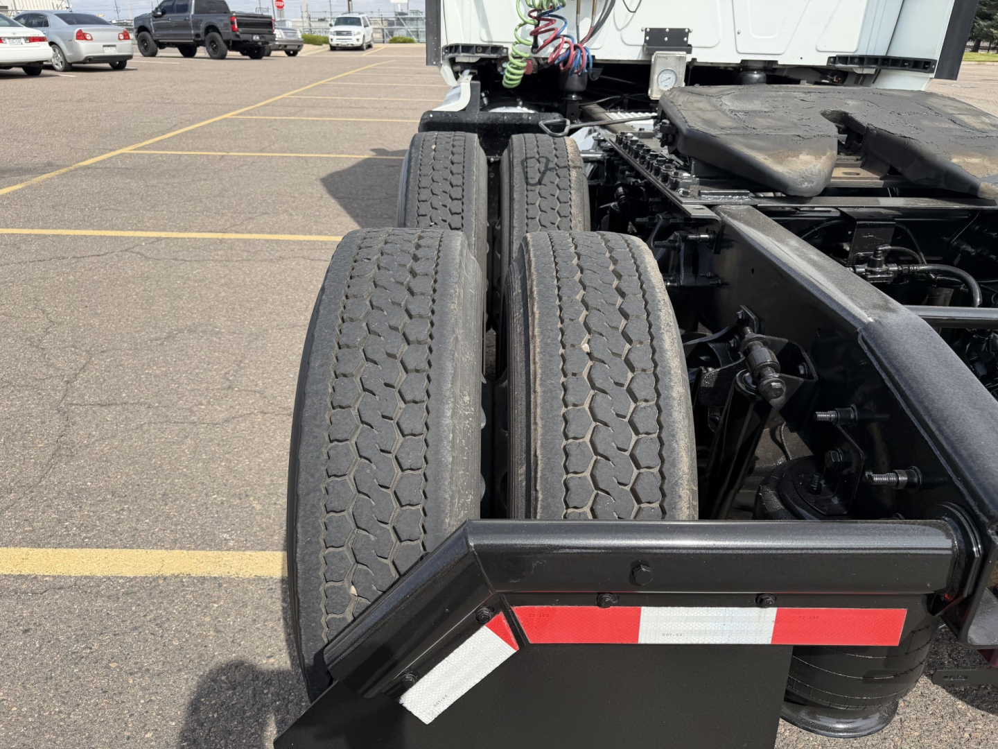 Trucking chassis rear view showing dual rear axles with tires and suspension, visible fuel lines and chassis frame under cab.