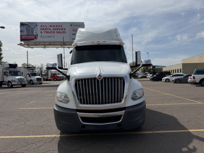 Front view of a white 2019 International LT625 semi-truck with prominent vertical grille, hood vents, large bumper, and sleeper cab; background shows dealership lot and other trucks.