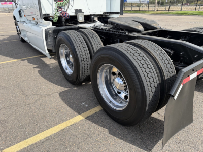 Truck rear chassis with dual rear axles and wheel tires, white cab, chrome rims, and black mud flaps visible.