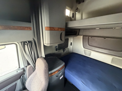 Interior cab view of a 2019 International LT625 sleeper truck showing bunk with blue mattress, storage cabinet, and window; red/brown trim accents.