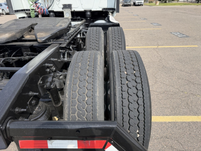 Truck chassis with dual rear axles and rubber tires; view shows suspension, frame, and drivetrain under a 2019 International LT625 in a parking lot.