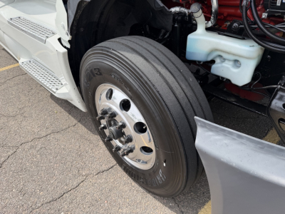 Truck front wheel and engine bay showing dual rear truck tire, chrome hub, white plastic coolant reservoir cap, and part of the engine block.