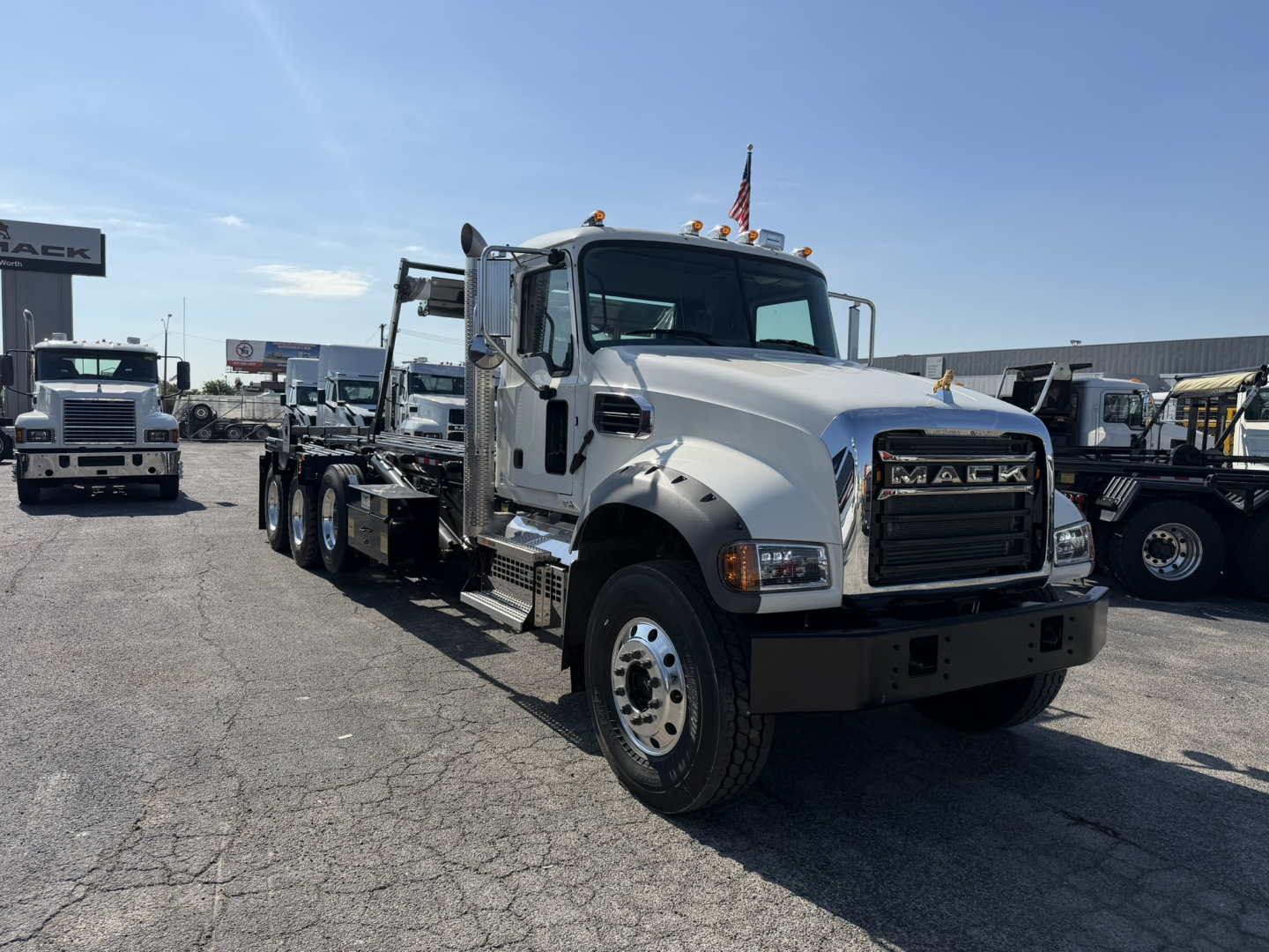 Truck image showing a white 2026 Mack GR64F rolloff truck in a dealership lot with multiple trucks in background.