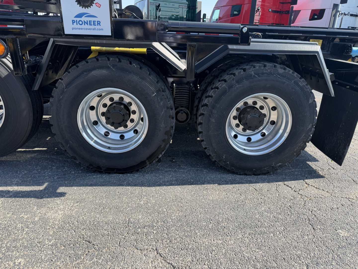 Mack GR64F truck side view showing dual rear axles with large off-road tires and rims, chassis components, and a rollover bed; some branding and stock data visible.