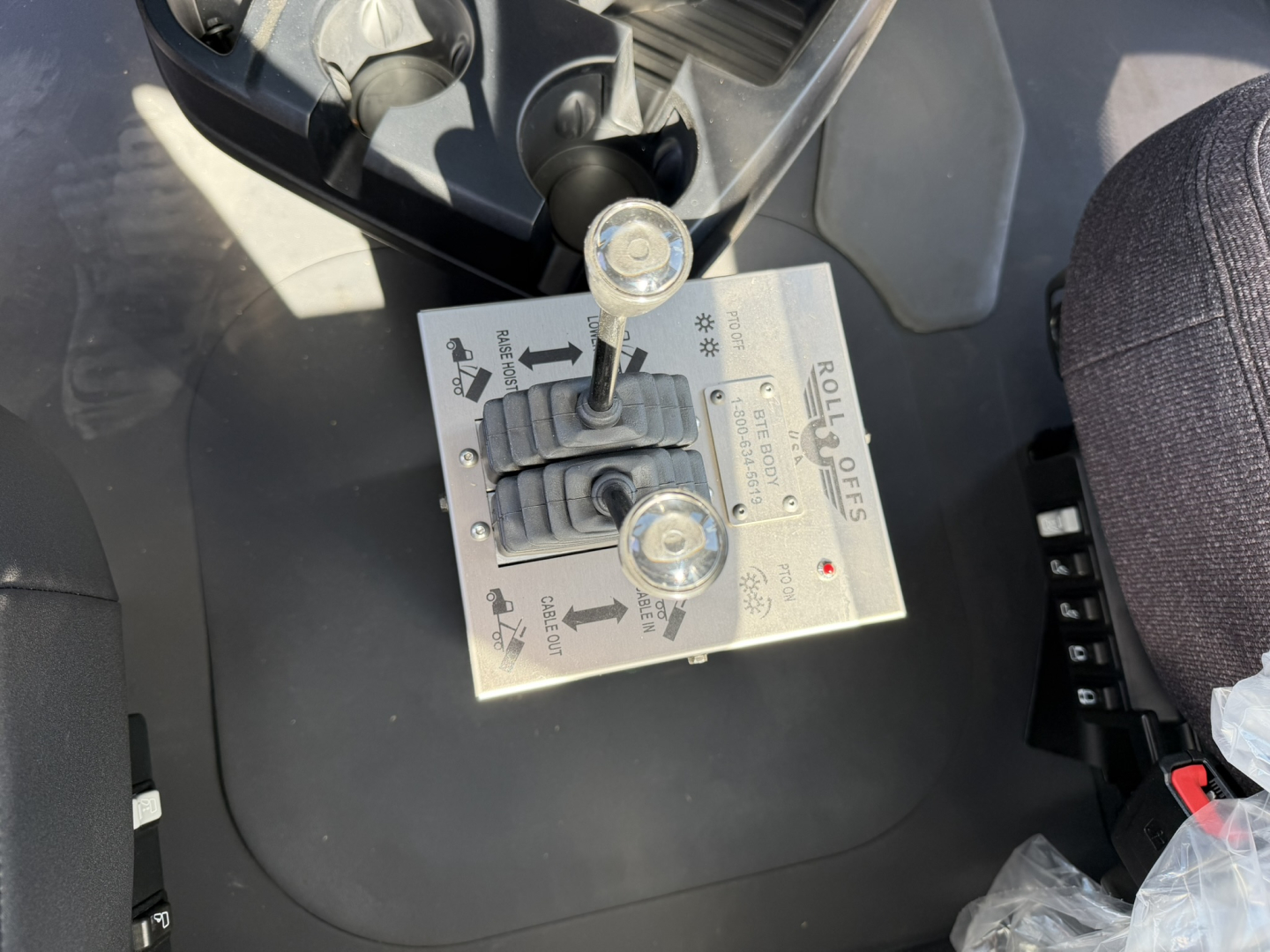 Rolloff control panel with levers and knobs mounted on a Mack GR64F cab interior showing arrows, labels, and screw terminals.