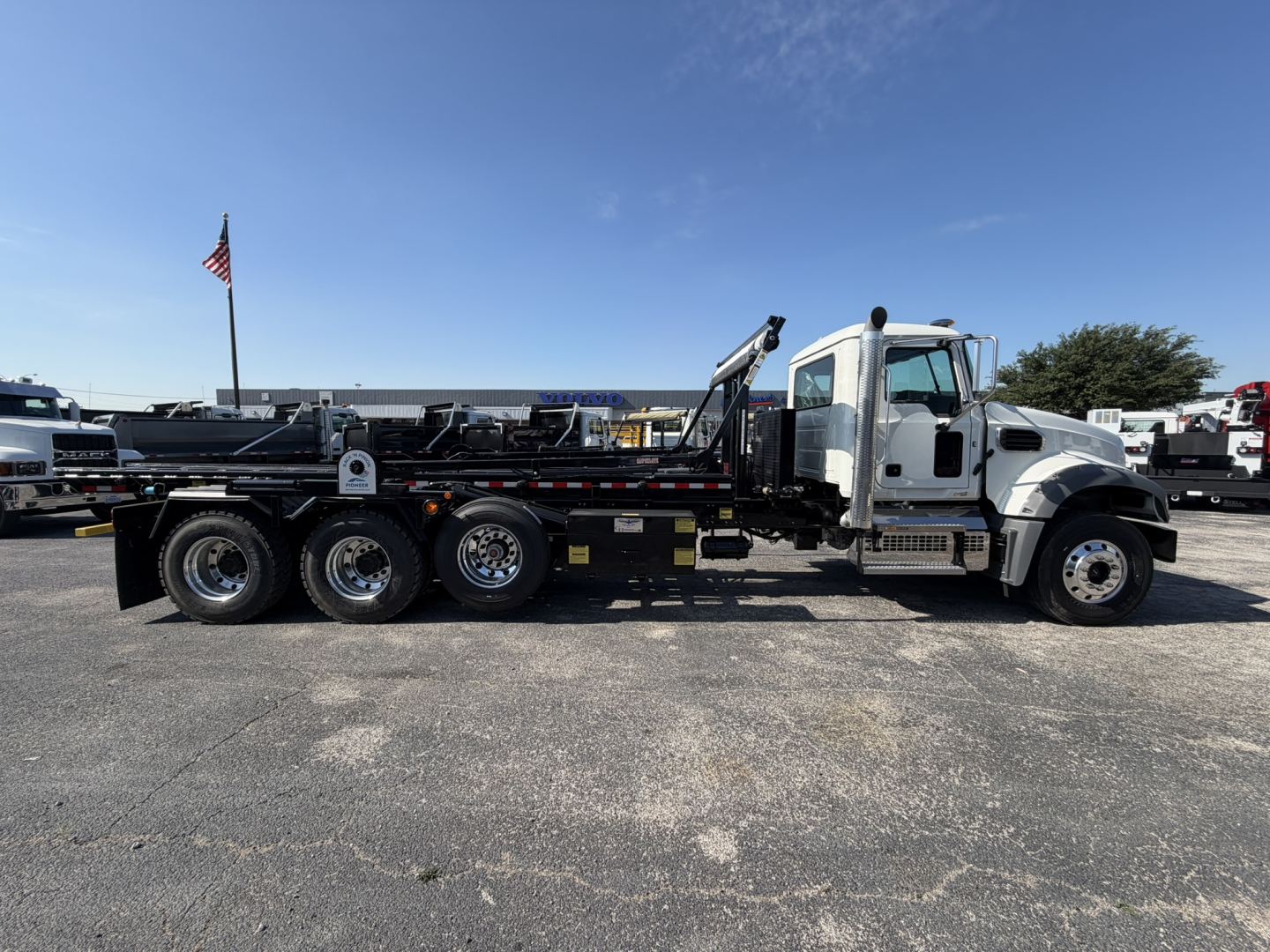Mack GR64F roll-off truck in side profile showing cab, crane, and multiple axles. No legible text on decals visible in image.