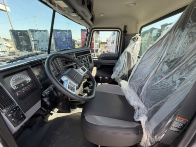 Cab interior of a 2026 Mack GR64F rolloff truck showing steering wheel, dashboard, driver seat with plastic cover, passenger seat, and shift levers.