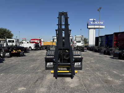 Mack GR64F roll-off truck chassis and hydraulic arm seen from front center in a dealership lot with other trucks in background.
