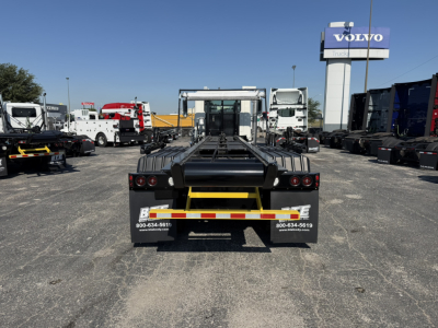 Rear view of a Mack GR64F roll-off truck showing lashing bars and rear bumper with warning lights and a small text label.