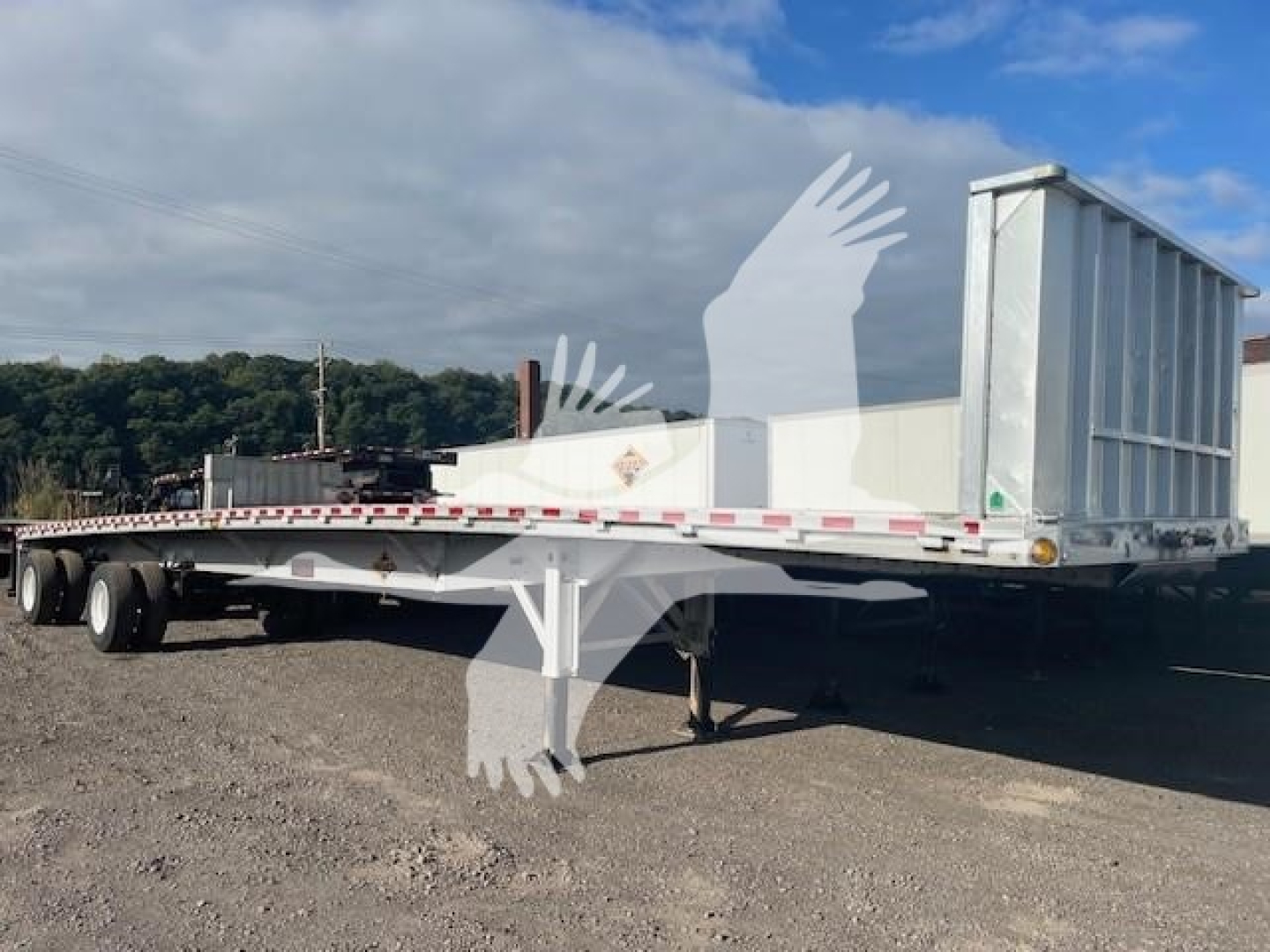Flatbed trailer showing midsection and rear with a deck and tandem axles, 2020 Reitnouer Big Bubba model, white exterior, trailer ramp and rear structures visible.