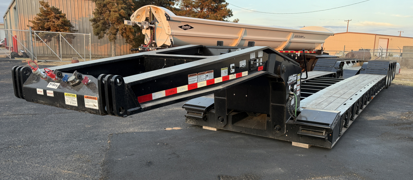 Load King 554-Quad-9' wide 24' LDH lowboy trailer with extended gooseneck and multiple axles, black with safety decals and reflective tape.