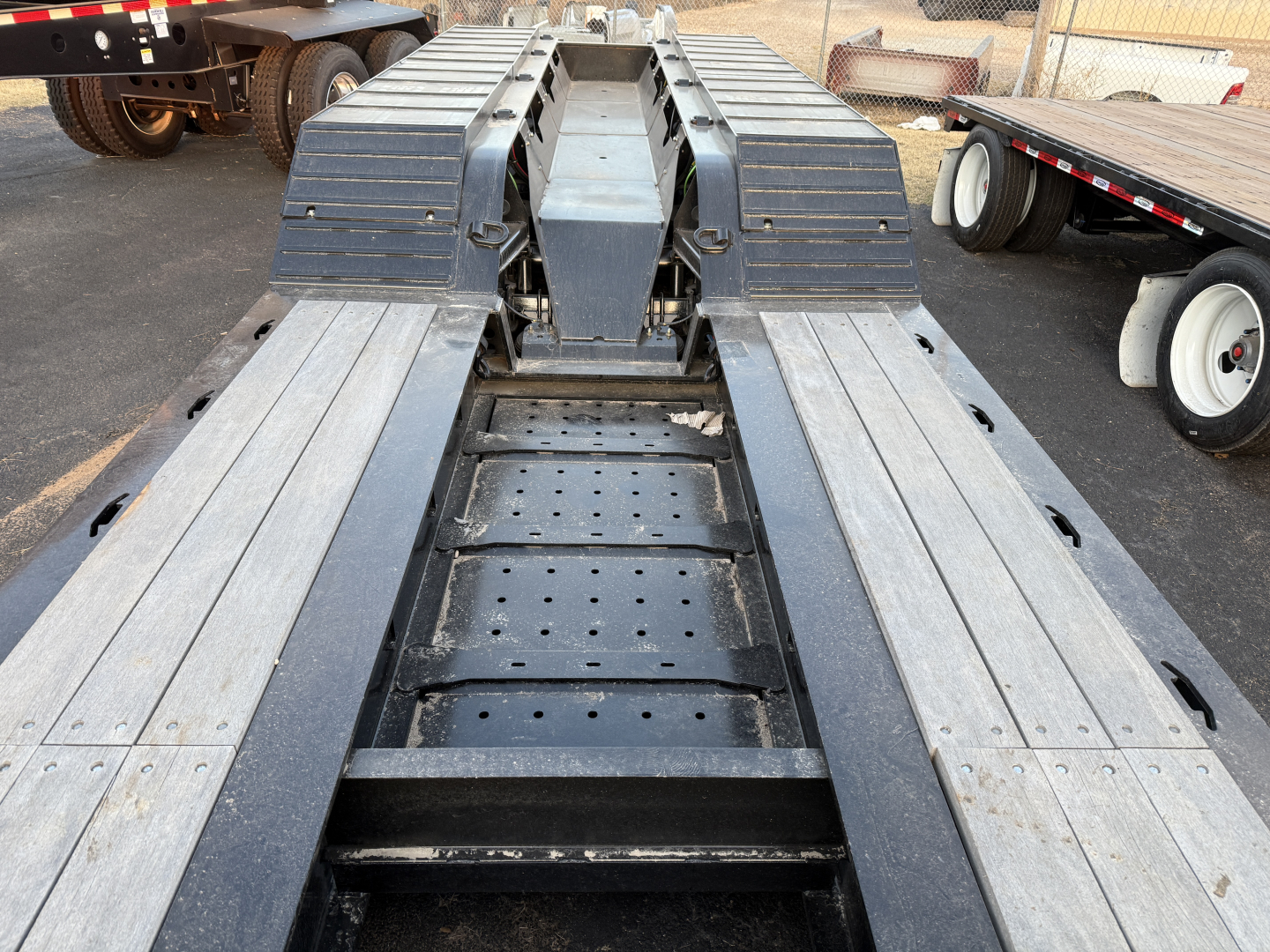 Trailer deck and wheel wells of a Load King lowboy trailer viewed from the center, showing aluminum deck planks, cross-members, and fender/dual rail assemblies.