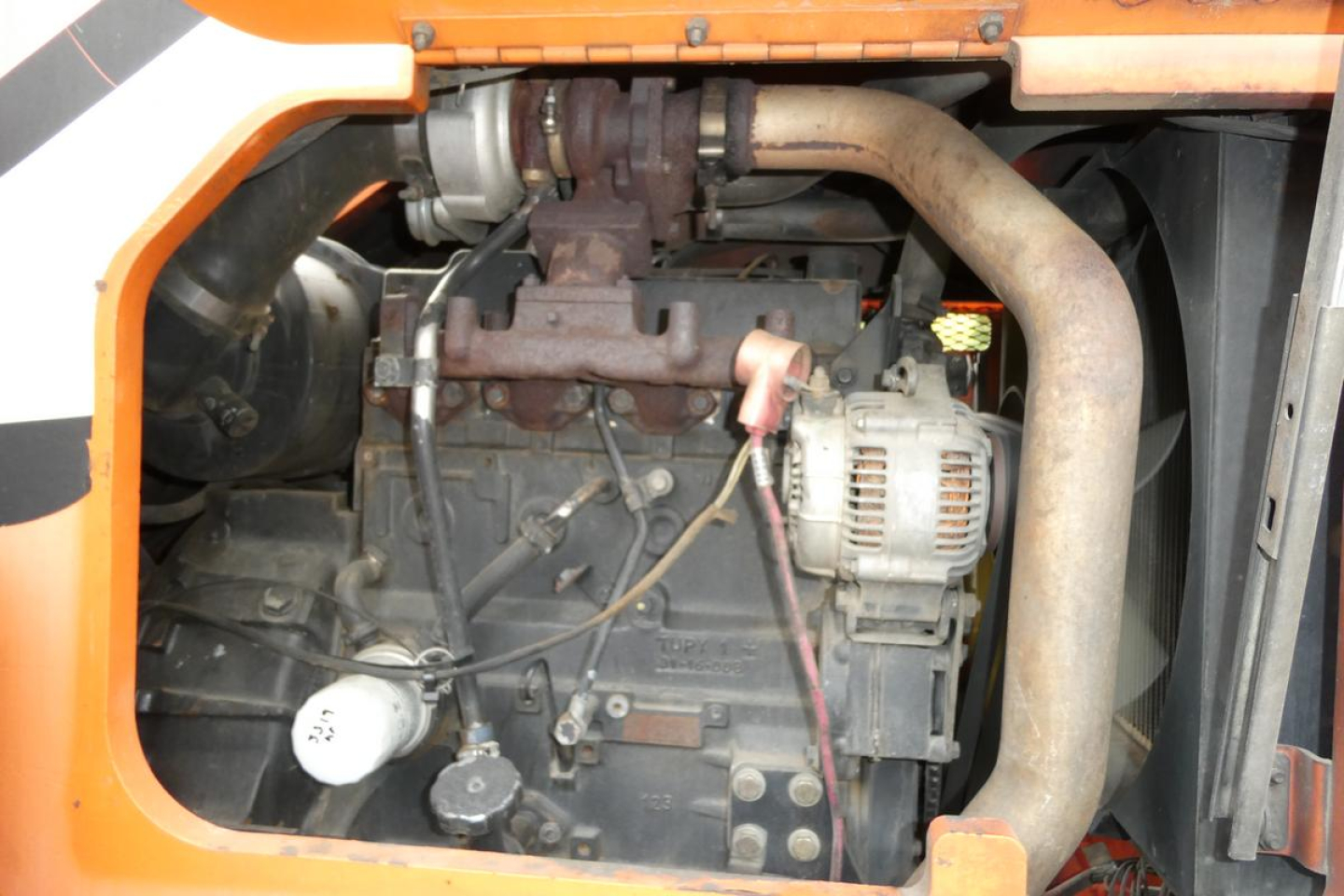JLG 6042 telehandler engine bay showing radiator hoses, turbo/engine block, alternator, and exhaust pipe with surrounding orange machine frame.