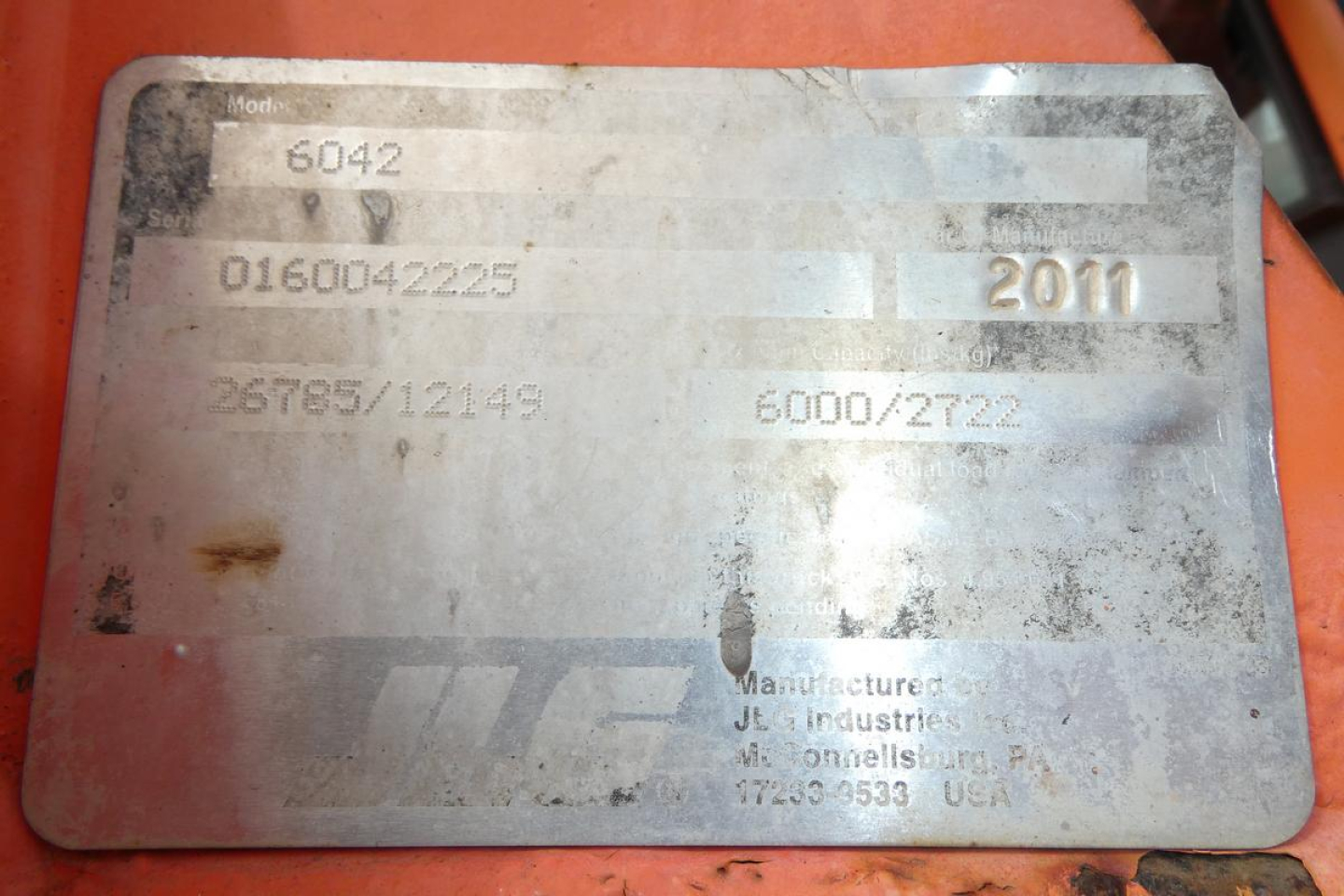 Label plate on JLG 6042 telehandler showing model number 6042, year 2011, VIN 0160042225, stock 1012261 with faded text and serials.