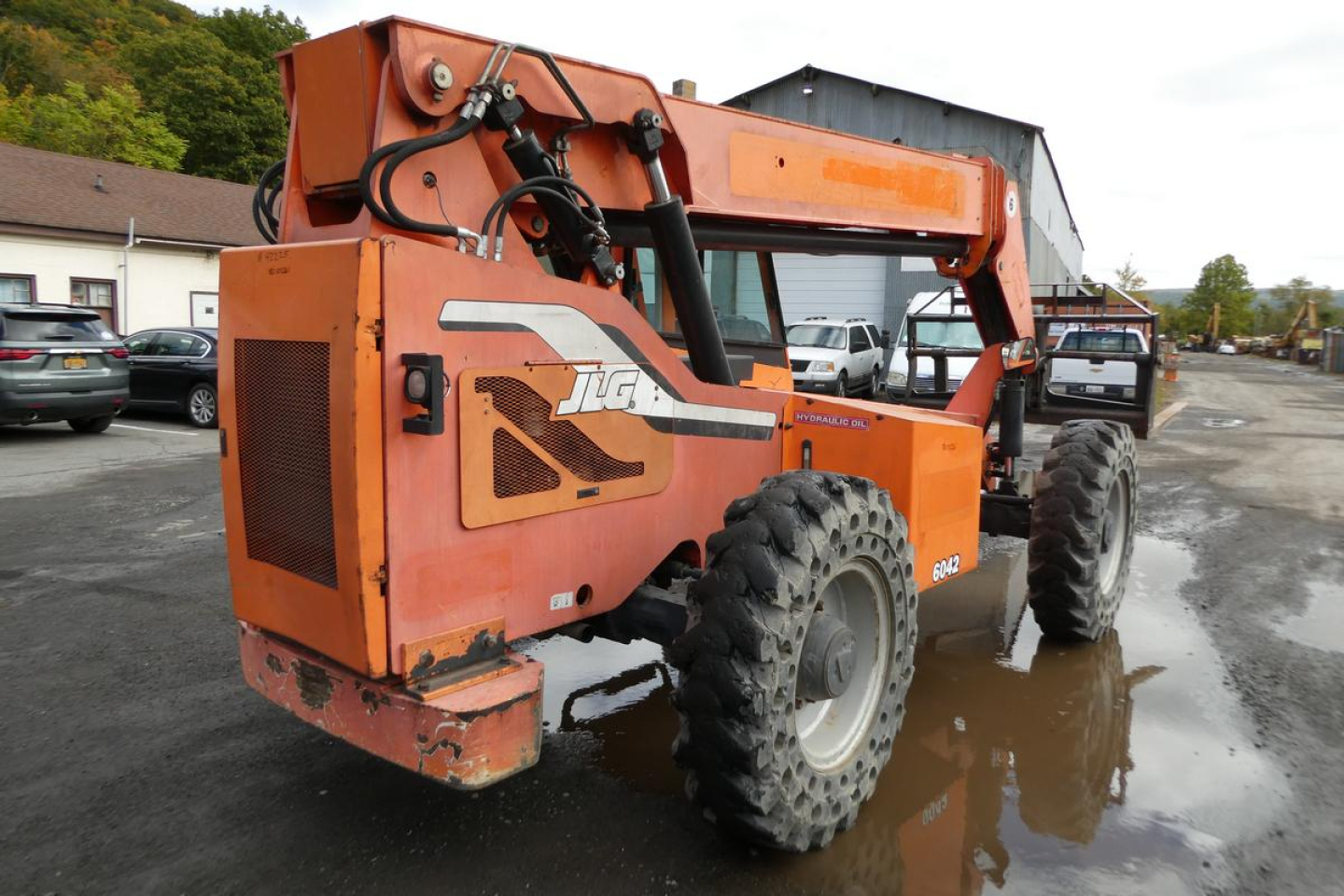 JLG 6042 telehandler in-view showing side profile and orange paint with sticker text and hydraulic boom components.