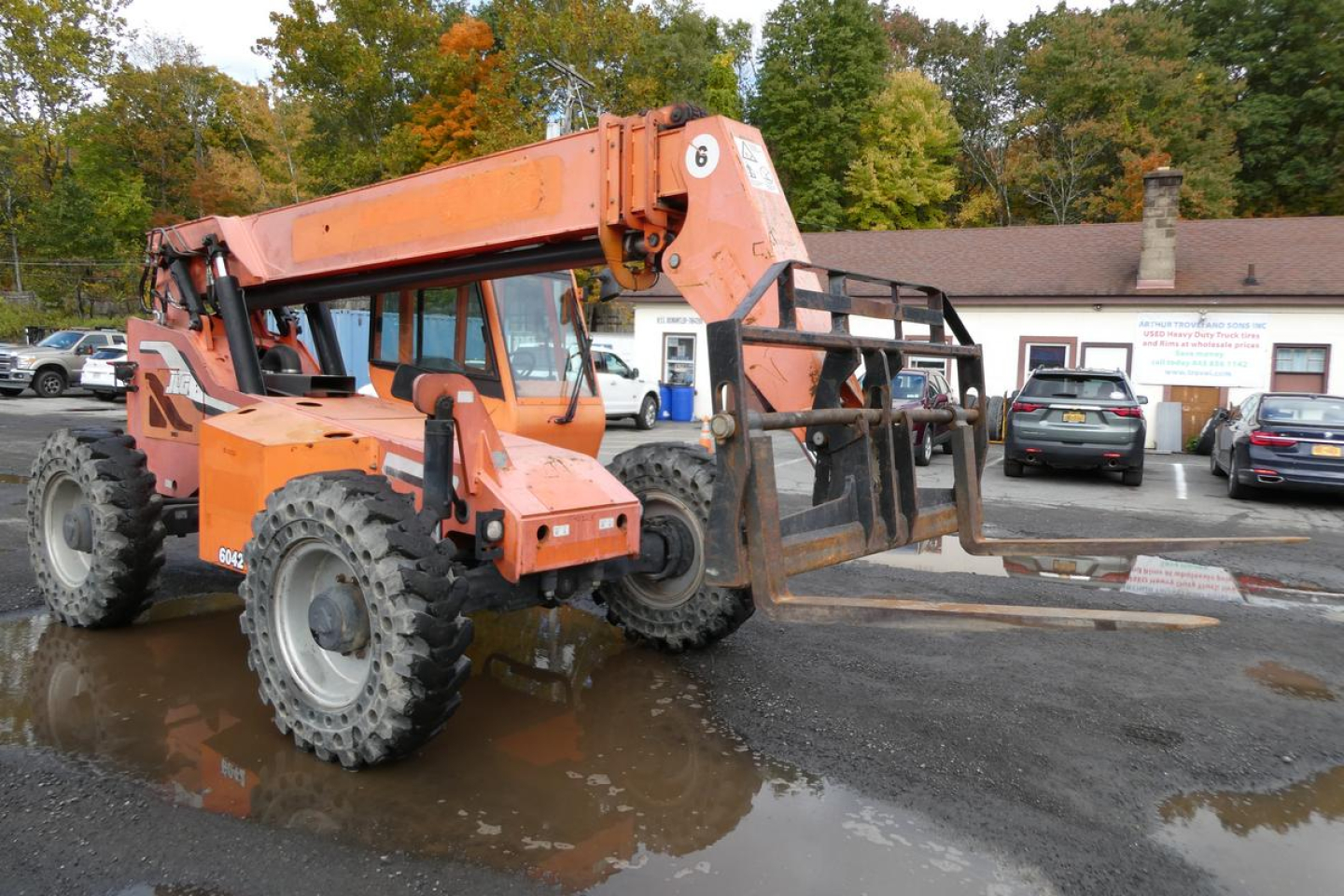Orange JLG 6042 telescopic boom lift in a parking lot with crawler-style tires and extended arm; rear platform and operator cab visible.