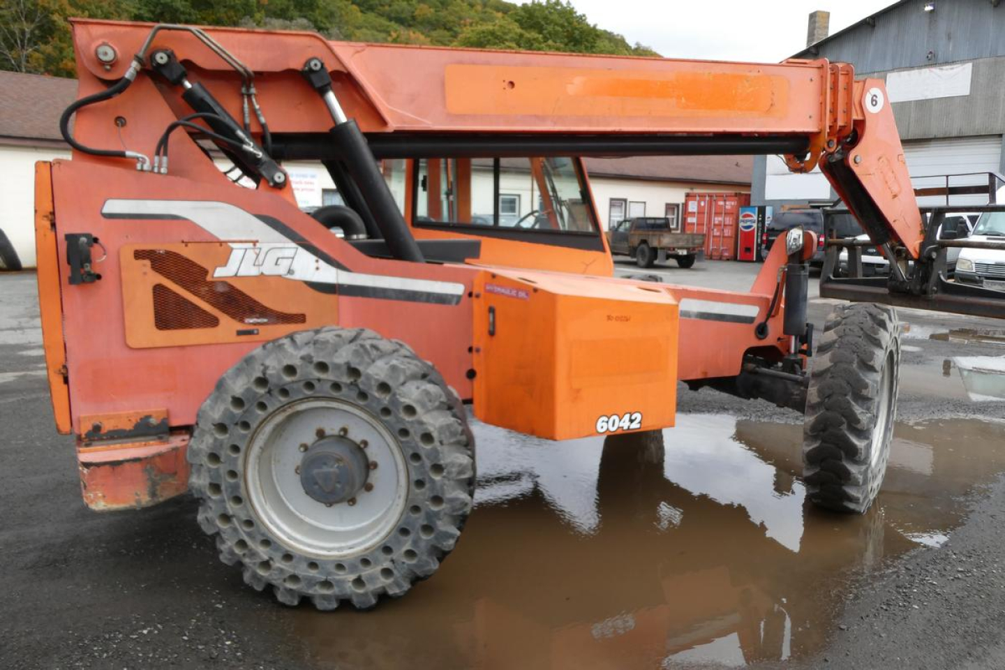 Orange JLG 6042 telescopic boom lift in service position showing chassis, large off-road tires, and hydraulic boom arm with stabilizers.