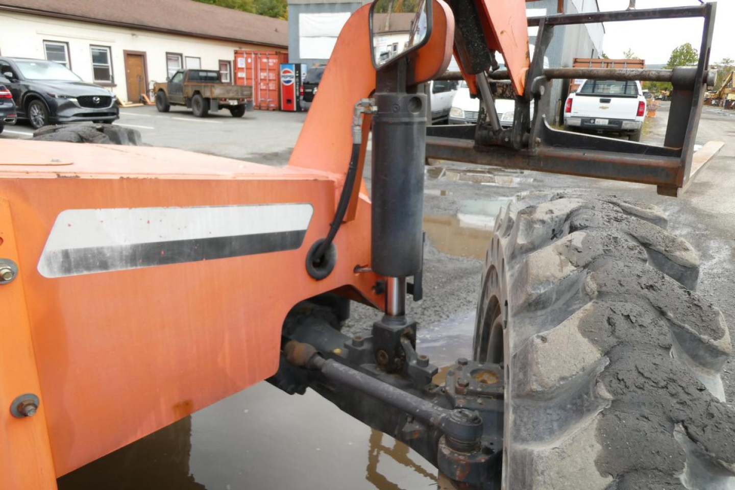 JLG 6042 telescopic forklift side view showing hydraulic strut and wheel, orange body with white stripe label.