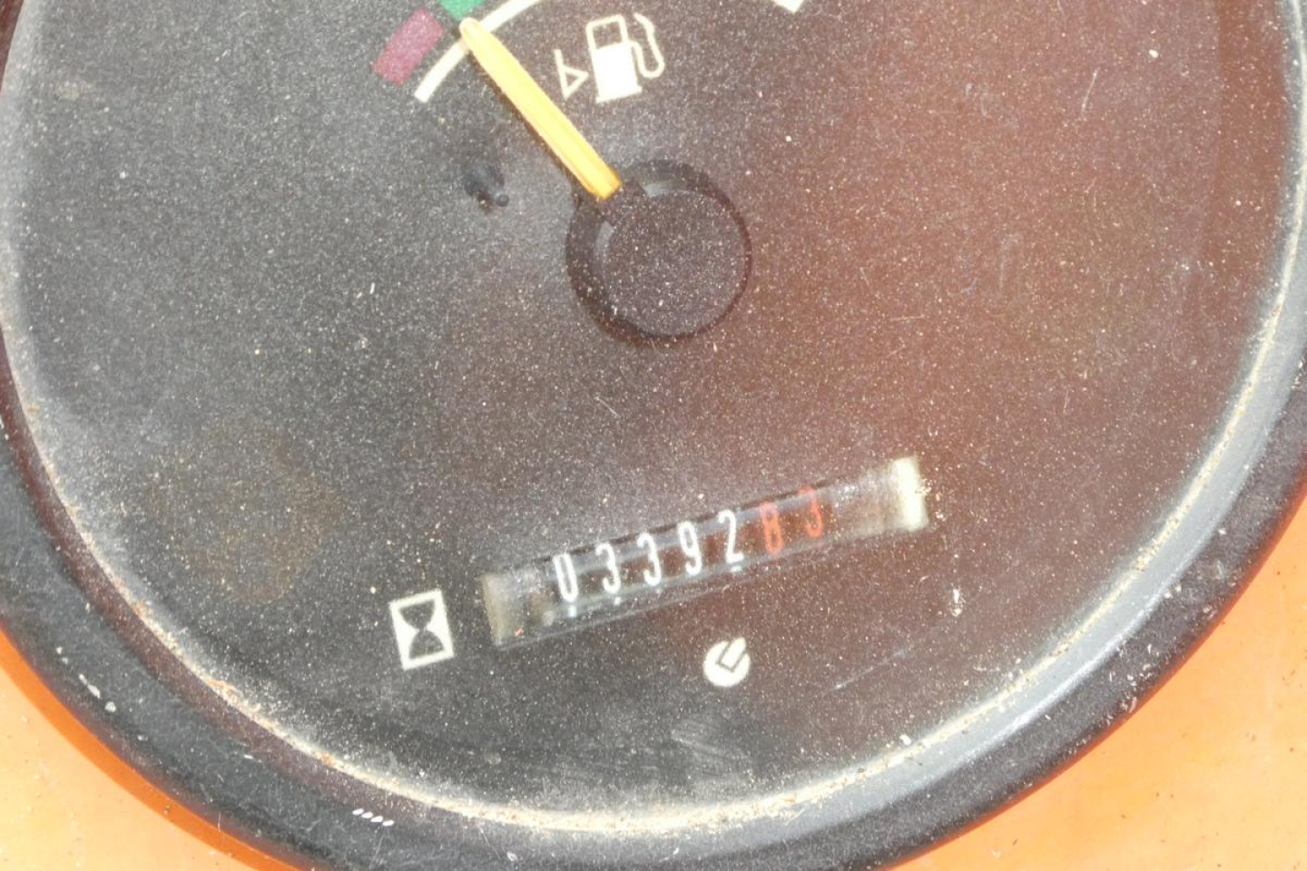 Dial gauge with numeric odometer-like readout and a colored pointer; circular black panel with faint icons and a small rectangular serial label.