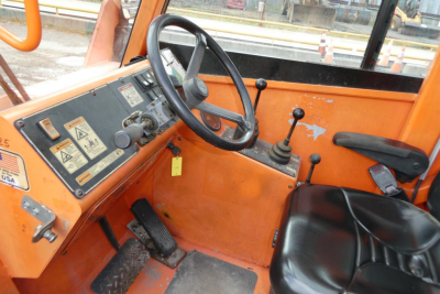 Operator cabin of a JLG 6042 telescopic forklift showing steering wheel, control levers, and orange panels with warning labels.