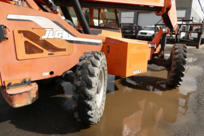JLG 6042 telescopic boom lift in service showing orange chassis and large off-road tires with JLG logo visible