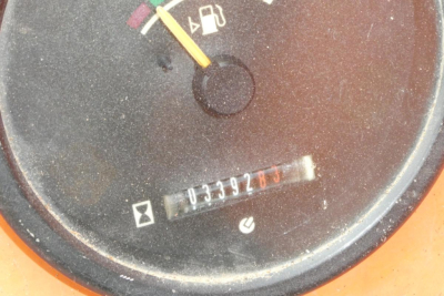 Dial gauge with numeric odometer-like readout and a colored pointer; circular black panel with faint icons and a small rectangular serial label.