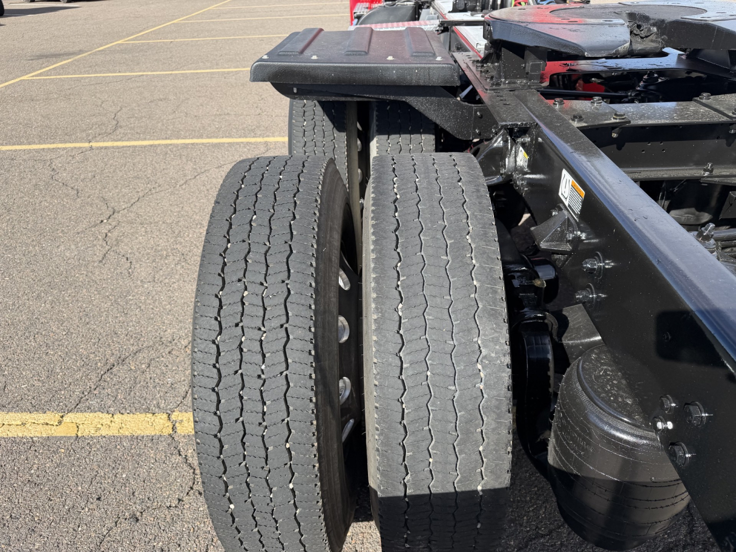 Kenworth T880 chassis with dual rear axles and tires visible, part of truck frame in a parking lot.