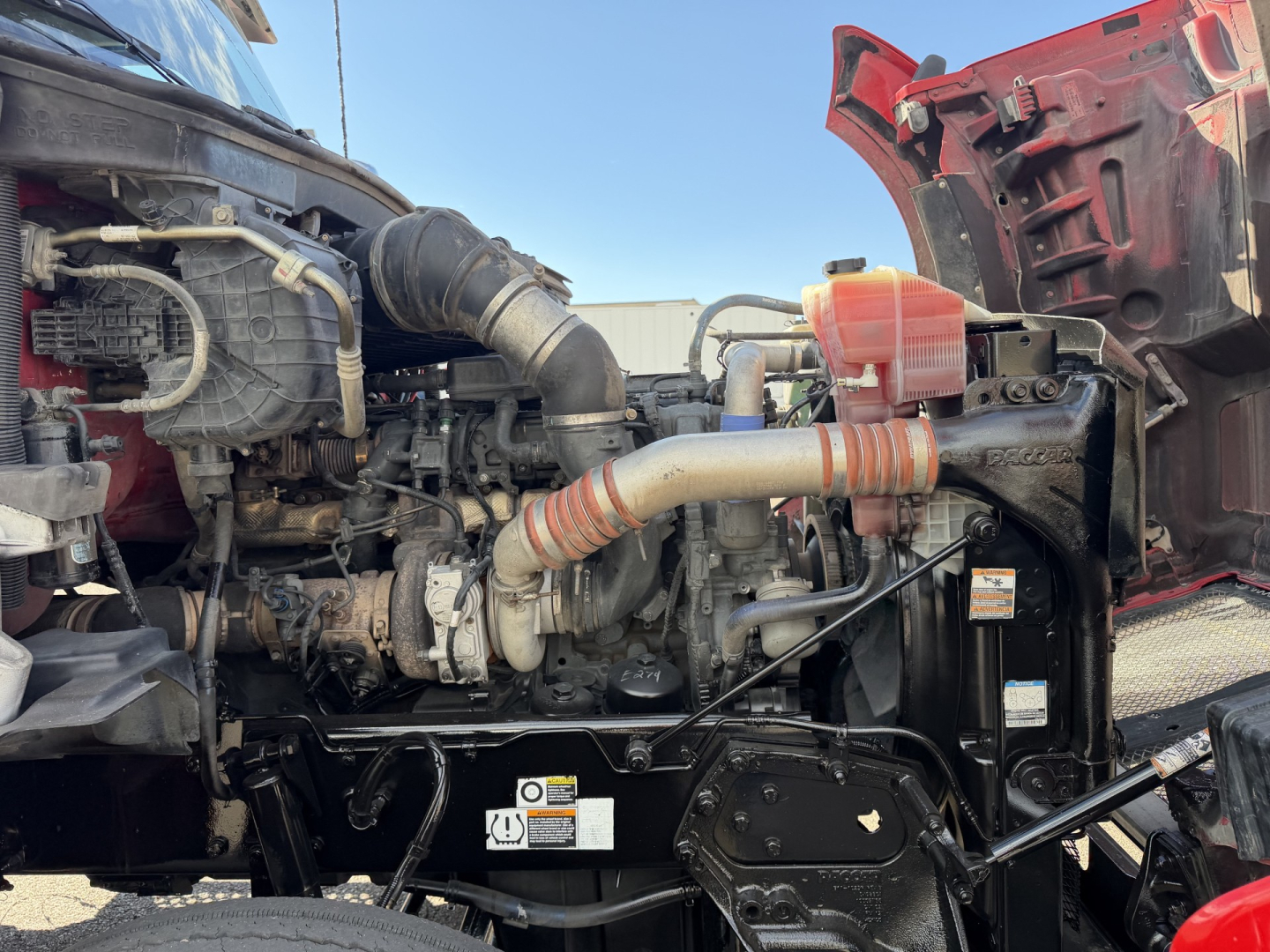 Kenworth T880 engine bay with exposed components including hoses, radiator, and intake, showing the front-right section of the engine and red hood interior.