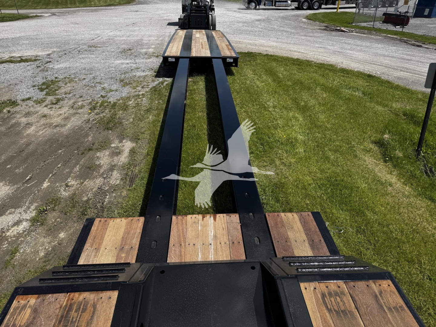 Trailer frame showing long lowboy chassis with dual steel beams and wooden deck sections in between, viewed from the front toward the tractor hitch.