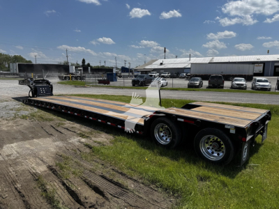 Tow trailer on a grassy lot showing a lowboy trailer with wood deck and dual-axle configuration.