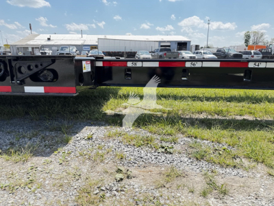 Fontaine lowboy trailer side with numbered ramps '58' '56' '54' and black painted frame; grassy ground in foreground and truck yard in background.