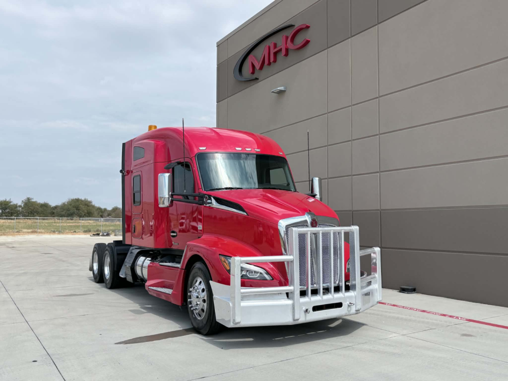 Kenworth T680 tractor in red color with chrome grille and bumper, parked in front of MH C building.
