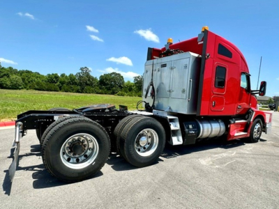 Kenworth T680 tractor in red cab with sleeper, side view showing rear dual wheels, fuel tanks, and chrome exhaust, exterior details visible.
