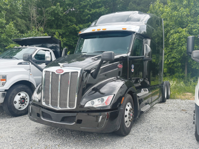 Peterbilt 579 conventional sleeper tractor in black, front view, chrome grille, daytime running lights, side mirrors, and dual rear axles.