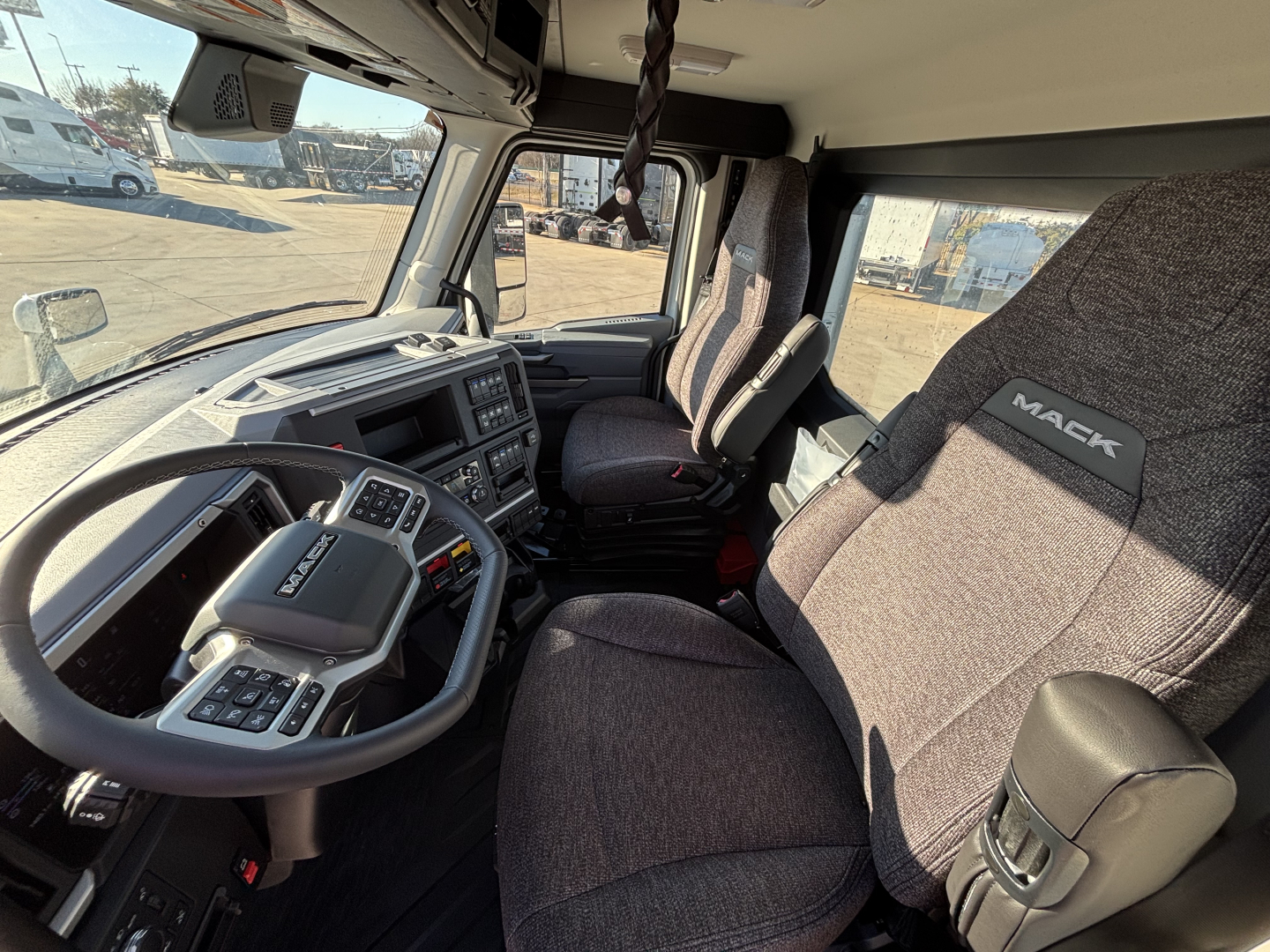 Truck cab interior showing steering wheel, dashboard, and Mack-branded seat in a new Mack PR64T tractor.